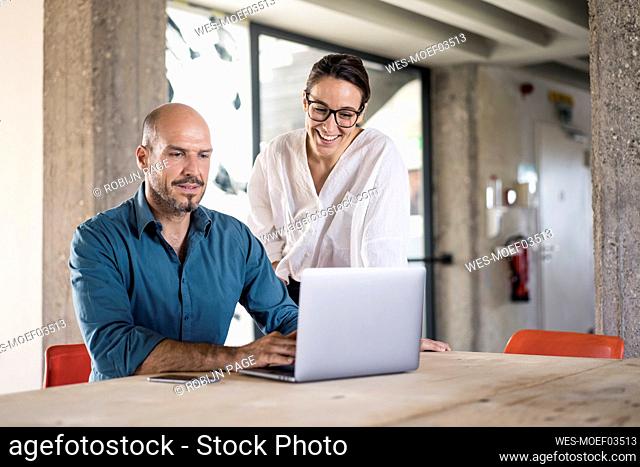 Businesswoman using laptop by woman standing at table in office