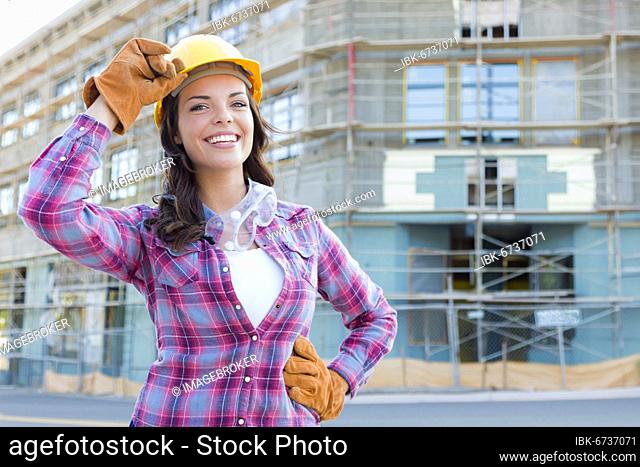 Portrait of young attractive female construction worker wearing gloves, hard hat and protective goggles at construction site