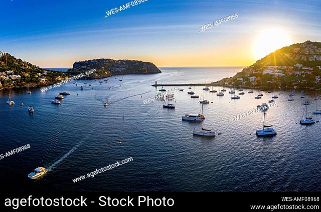 Spain, Balearic Islands, Andratx, Helicopter view of boats sailing near shore of coastal town at sunset