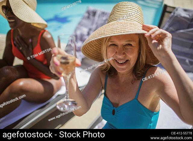 Portrait happy senior woman drinking champagne at sunny poolside