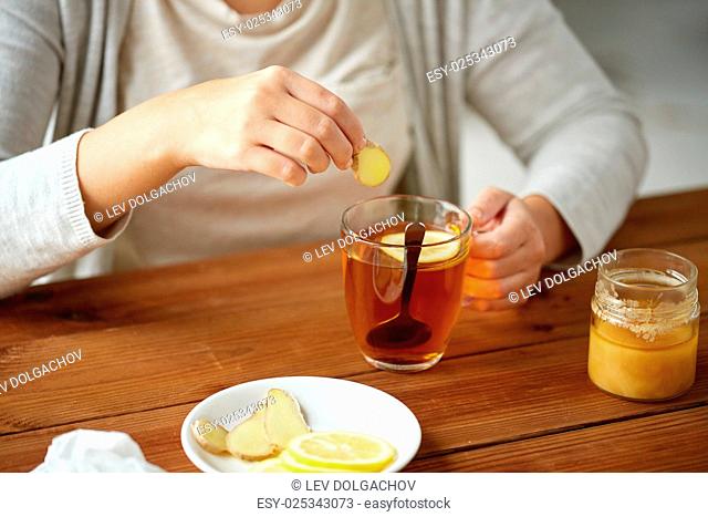 health, traditional medicine and ethnoscience concept - close up of woman adding ginger to tea cup with lemon and honey