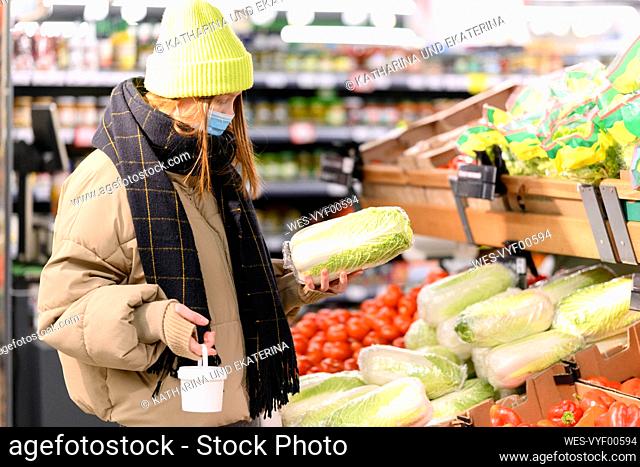 Young woman buying vegetables at supermarket during COVID-19