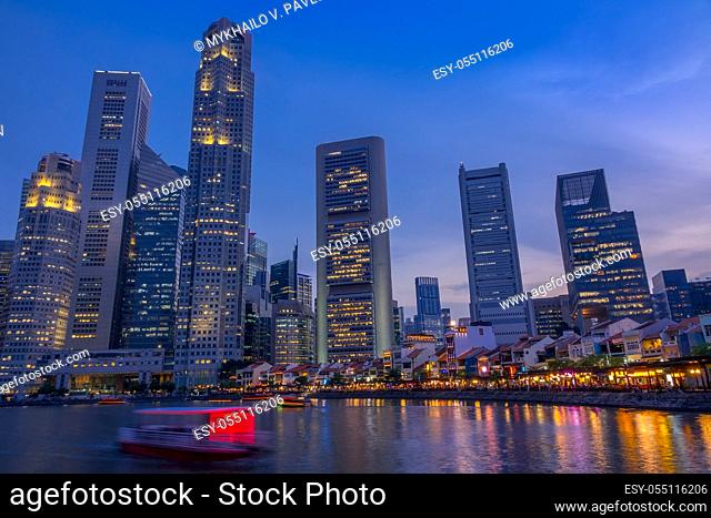 Singapore. Quay with cafes and skyscrapers. Pleasure boats. Dusk