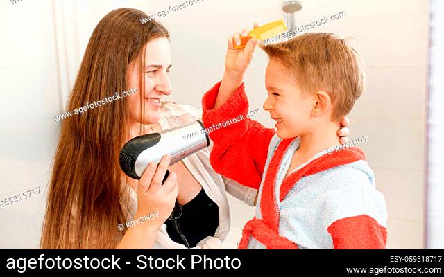 Young caring mother drying hair and looking on her little son in bathroom. Concept of child hygiene and health care at home