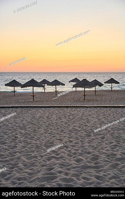 Empty beach at sunset in Comporta, Portugal with straw summer umbrellas