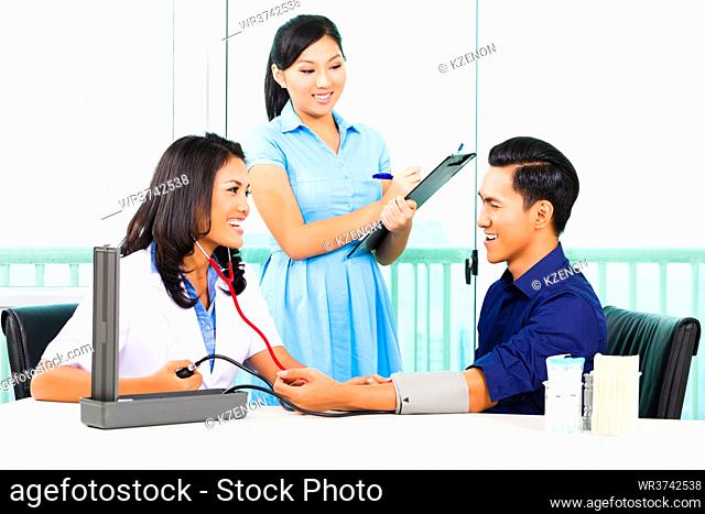 Asian female doctor check-up blood pressure on patient while nurse writing on clipboard