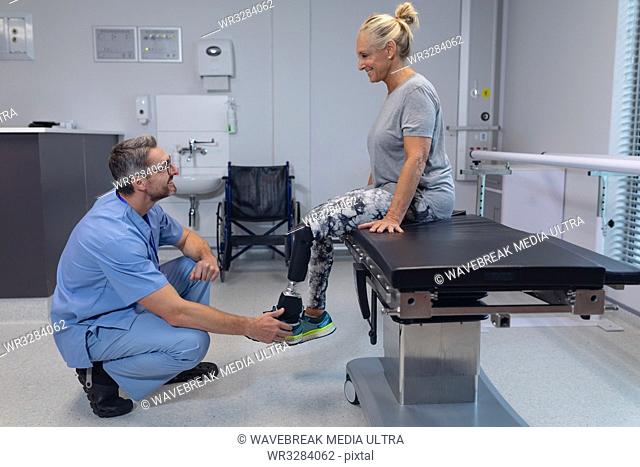 Side view of Caucasian male physiotherapist adjusting prosthetic leg of female patient in hospital