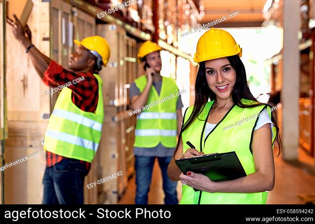 Portrait female white caucasian warehouse worker stand with clipboard and pen for inventory check with colleagues in large warehouse distribution background