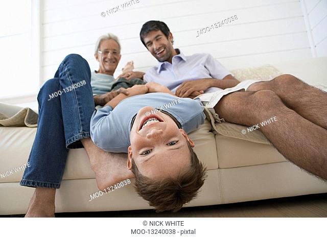 Boy hanging upside down off couch with father and grandfather sitting beside him