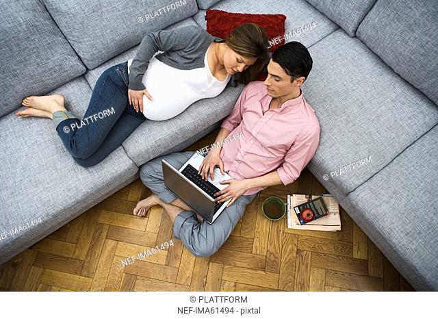 A man and a pregnant woman sitting in a couch using a laptop Sweden