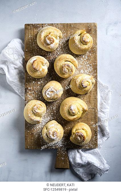 Vegan yeast spirals dusted with icing sugar on a wooden board (seen from above)