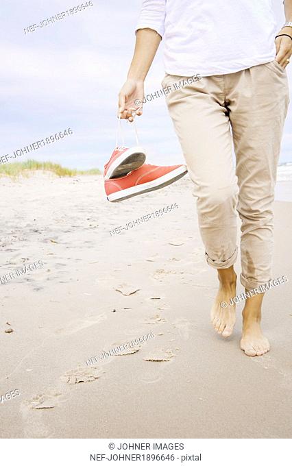 Woman on beach carrying shoes, close-up