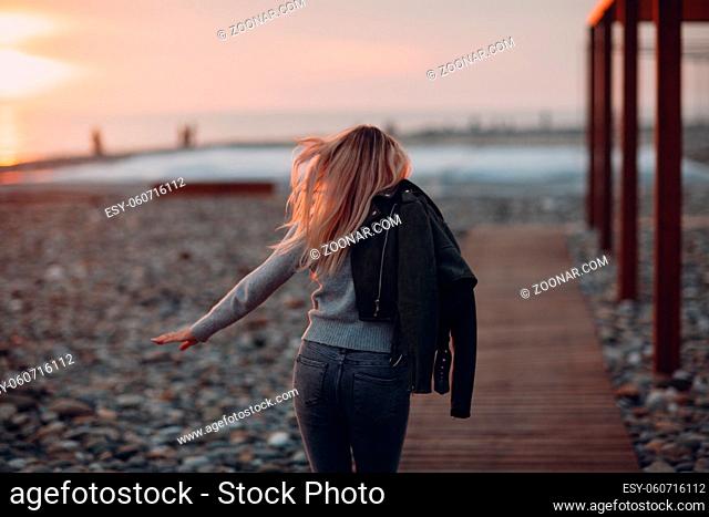 Young woman dressed in jeans and sweater on the seashore pebble beach