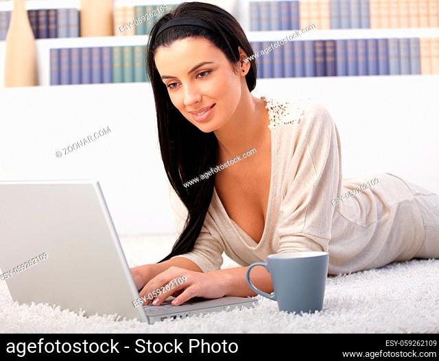 Woman browsing internet on laptop computer at home, lying on living room floor