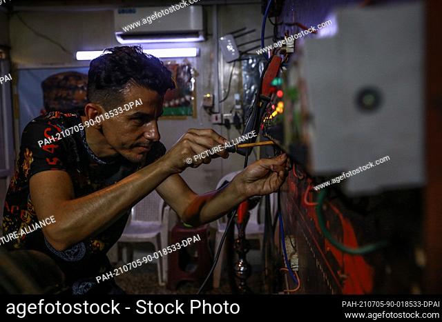 05 July 2021, Iraq, Baghdad: Ali Kazem, who owns a local private electricity generating station, connects wires and switches to transfer electricity to homes