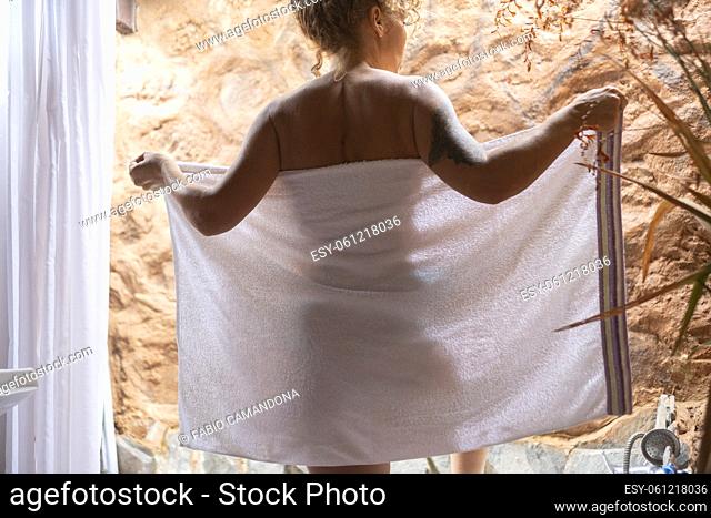Woman viewed from back ready to relax and wash herself in the bathroom opening white towels. Concept of body care and healthy lifestyle people at home or spa...