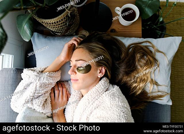Woman with under eyes patch sleeping on bed at home
