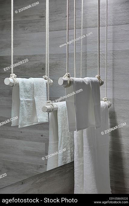 Hanging white wooden towel holders with white towels on the mirror background in the modern bathroom with gray wooden walls. Closeup. Vertical