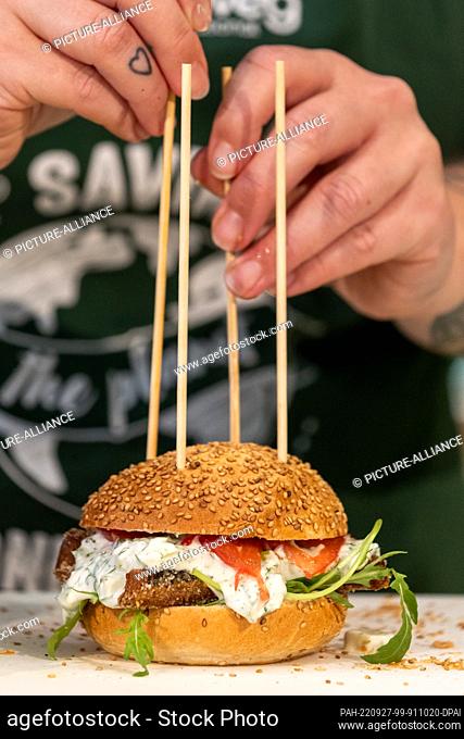 PRODUCTION - 27 July 2022, Bavaria, Nuremberg: A cook prepares burgers with onions, meat tomatoes, tartar sauce and breaded fish sticks without fish