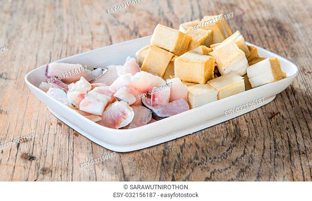 Meat, fish and tofu dish in white placed on a wooden table. Focus on fish