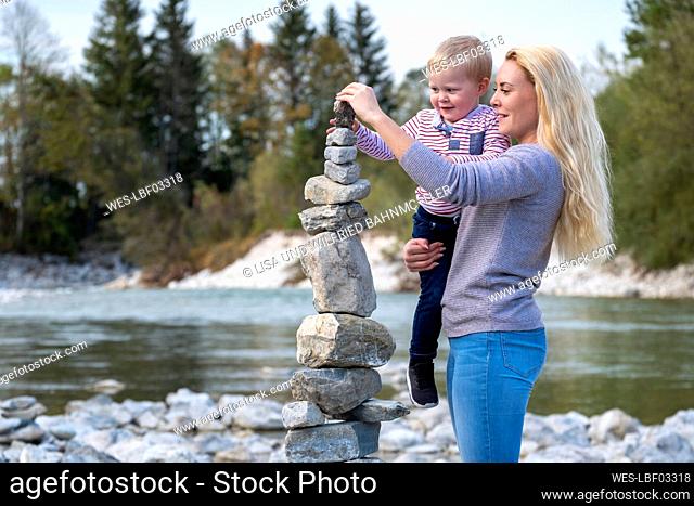 Mother carrying son while balancing stack of stones at riverside