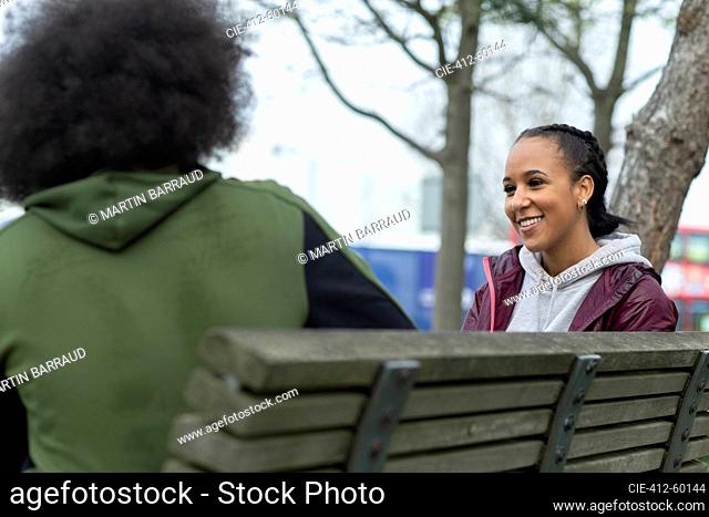 Happy young woman talking with friend on park bench
