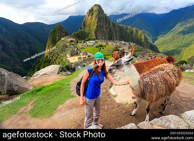 Young woman standing with friendly llamas at Machu Picchu overlook in Peru. In 2007 Machu Picchu was voted one of the New Seven Wonders of the World