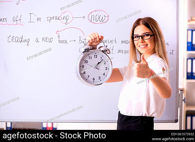 Young female english language teacher standing in front of the blackboard