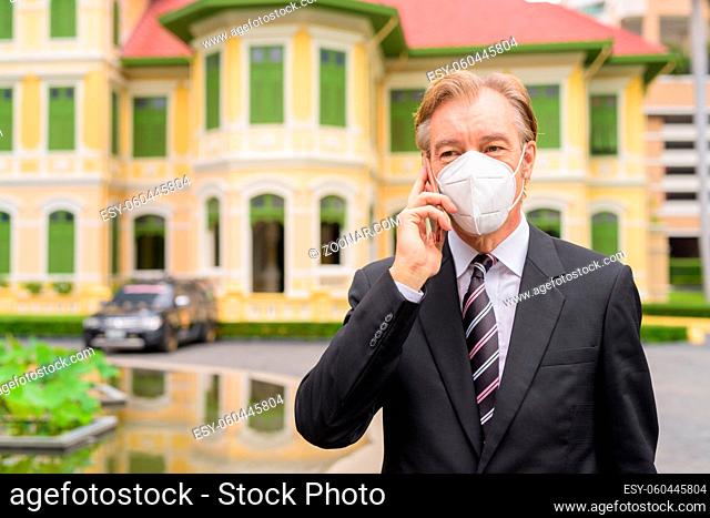 Portrait of mature businessman in suit with mask for protection from corona virus outbreak in the city streets outdoors