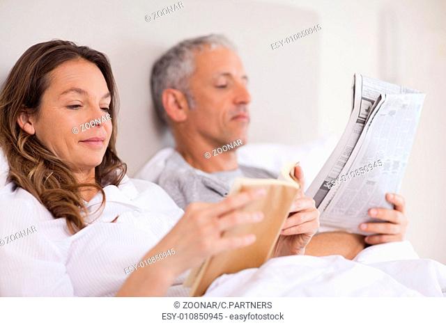 Woman reading a book while her husband is reading the news