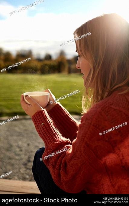 Young woman sitting on porch and drinking coffee