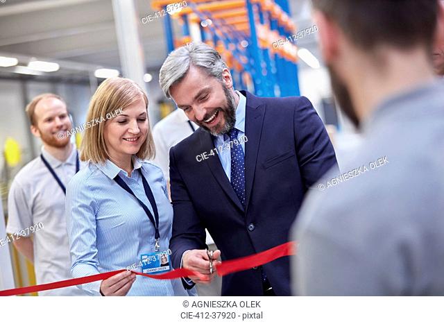 Businessman and businesswoman cutting ceremonial ribbon in fiber optics factory