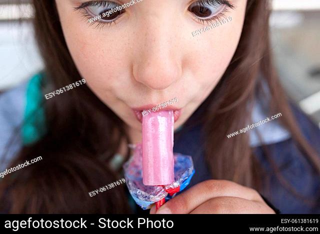 Little girl licking a whistle or melody pop. She is making a funny face