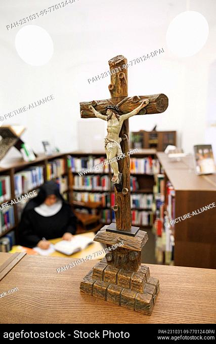 PRODUCTION - 20 October 2023, Lower Saxony, Osnabrück: Sister Josefine sits behind a cross in a posed situation in a room of the Osnabrück Diocesan Library