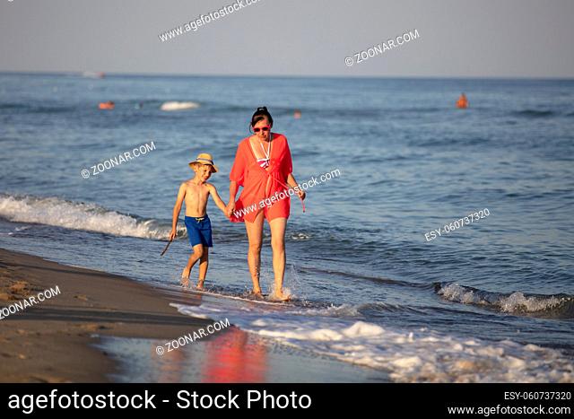 A woman with a child walks along the beach.Mom and son by the sea