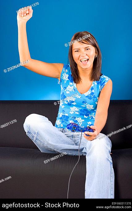 Young woman sitting on the black sofa with a computer pad in her hand. Blue background, in studio