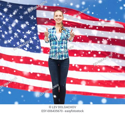 patriotism, education, gesture and people concept - smiling girl in casual clothes showing thumbs up over american flag and blue sky with snow background