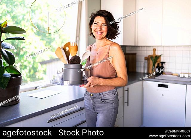 Happy woman holding cooking utensils in container on tray at home