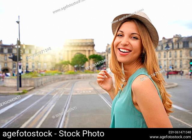 Portrait of smiling young tourist woman looks at camera on Pont de pierre bridge in Bordeaux, France