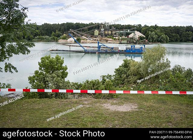 11 July 2020, Hessen, Babenhausen: Barrier tape hangs from the edge of the steep bank at a quarry pond on the outskirts of the southern Hessian town