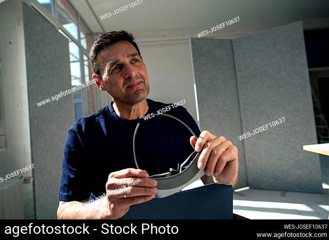 Thoughtful businessman holding virtual reality headset sitting at office