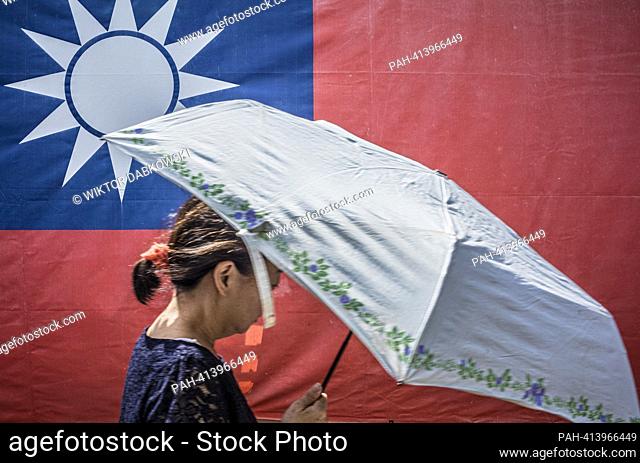 A woman holding umbrella in her hand walks past a giant banner with the flag of the Republic of China in downtown in Taipei
