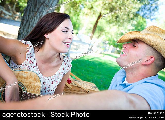 Young adult girl playing guitar with boyfriend in the park