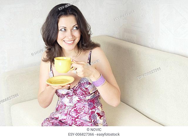 Smiling lady with teacup sitting on a sofa and looking aside