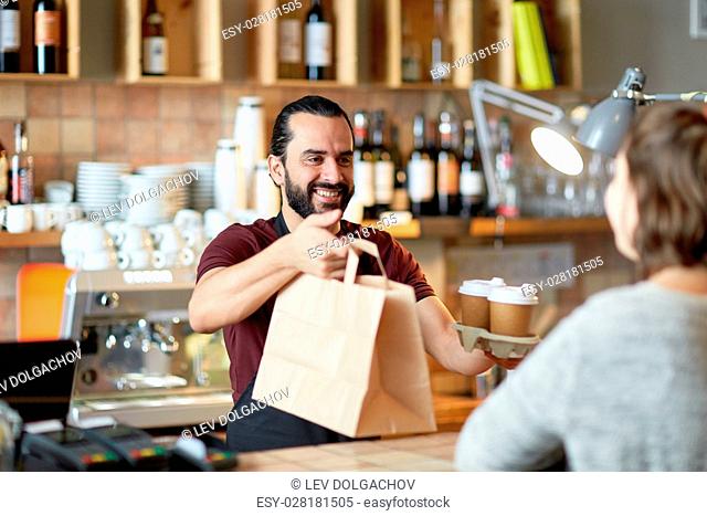 small business, people, takeaway and service concept - happy man or waiter giving bag and paper cups with hot drinks to customer at coffee shop