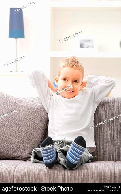 Happy relaxed young boy wearing white t-shirt, sitting at couch, looking at camera, smiling