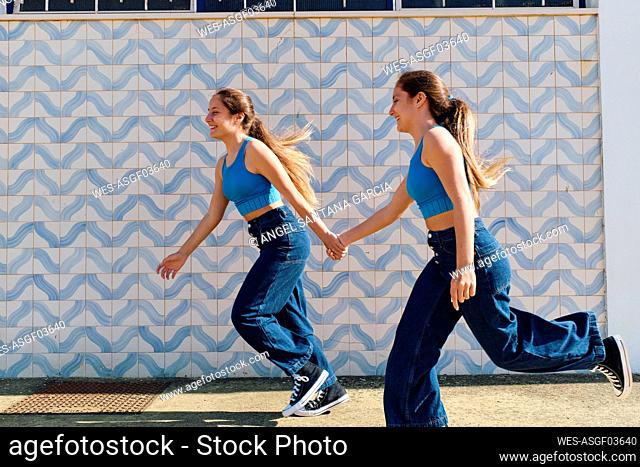 Sisters holding hands and running in front of wall