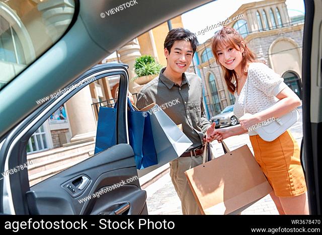Young couples with a shopping bag standing beside the car