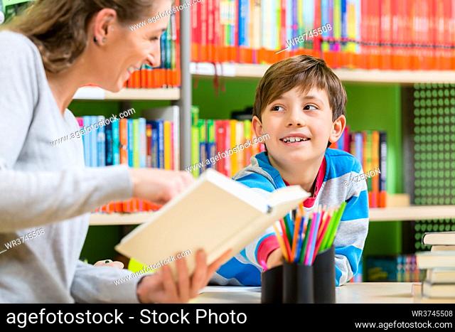 Mother reading book from library to her son turning a page