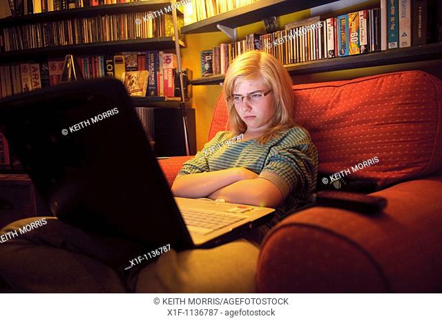A fifteen year old teenage girl viewing her Facebook page on her laptop computer at home UK